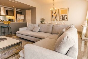 A modern living room with a sectional sofa, a coffee table, and a dining area with a chandelier. - Apto 33H en YOO, vista a la ciudad con 1 recamara (Panamá)