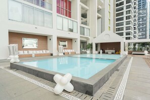 Una piscina con sillas de descanso y un edificio moderno con balcones.