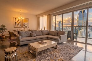 A modern living room with a large sofa, a coffee table, and a city view through floor-to-ceiling windows. - Apto 33H en YOO, vista a la ciudad con 1 recamara (Panamá)