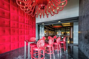 A modern interior with a red upholstered wall, a glass table with red chairs, and a chandelier. - Apto 33H en YOO, vista a la ciudad con 1 recamara (Panamá)