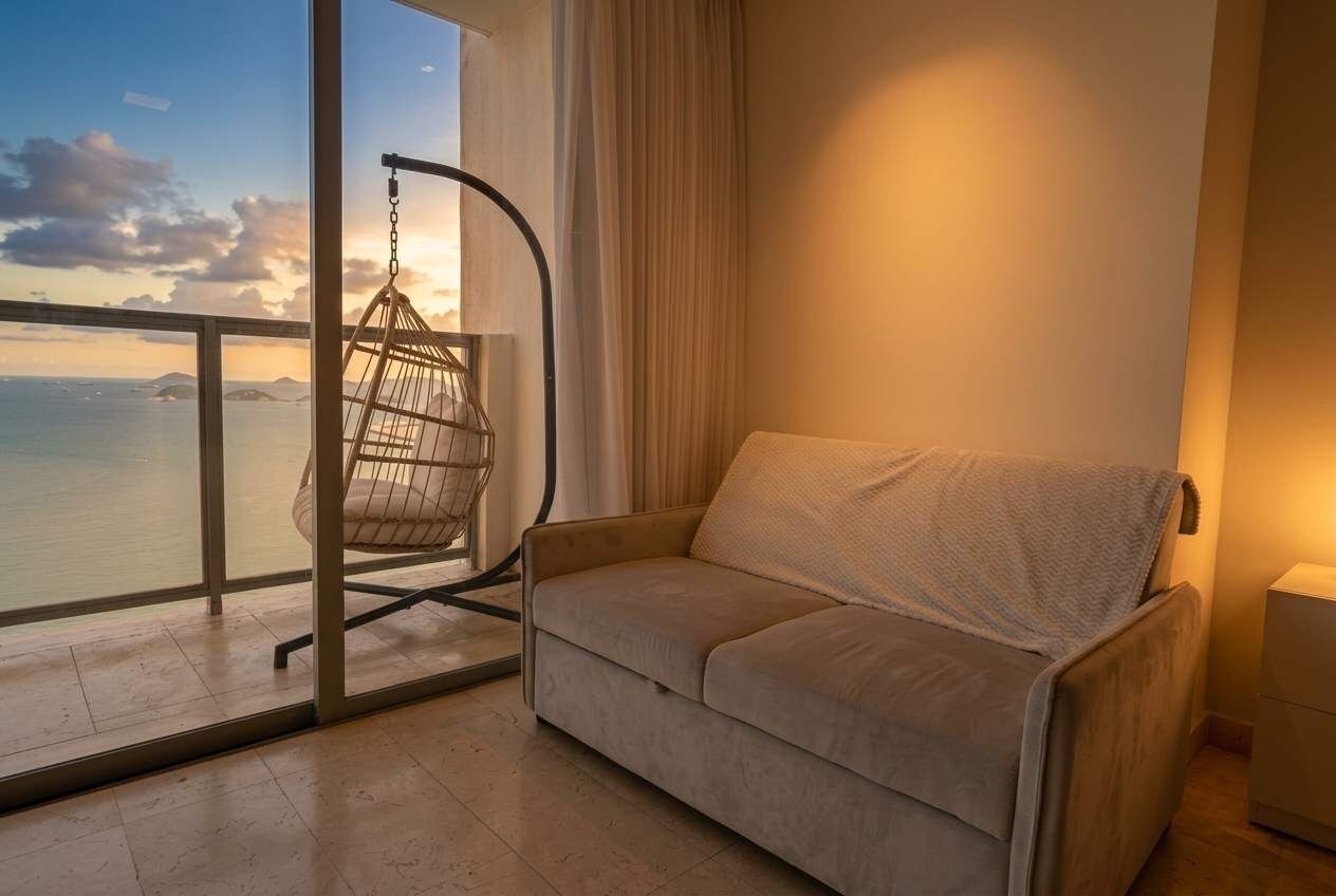 A balcony with a cushioned chair and a sofa, a view of the sea, and a curtain.