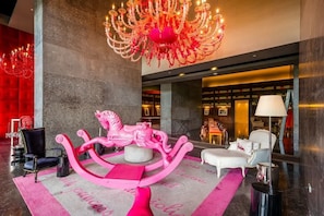 Un vestíbulo con una araña, una escultura de un caballo rosa y un sofá blanco.