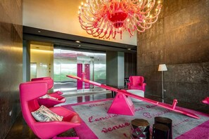 Un vestíbulo con una lámpara de araña moderna, sillas rosas y un suelo a cuadros con texto.