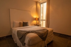 A hotel room with a large bed, a bedside table with a lamp, and a window with curtains. - 25J Lujoso Apto en YOO, vista al mar con 2 recámaras (Panamá)