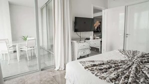 Ein Hotelzimmer mit einem Bett, einem Fernseher, einem Schreibtisch mit Stühlen und einer Glasschiebetür, die auf einen Balkon führt.