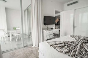 A hotel room with a bed, a television, a desk with chairs, and a sliding glass door leading to a balcony. - 25J Lujoso Apto en YOO, vista al mar con 2 recámaras (Panamá)