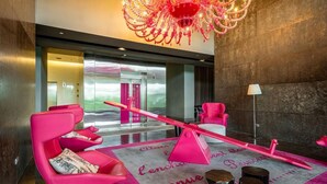 Eine moderne Lobby mit einer Kandelaber, rosa Stühlen, einer Wippe und einem Teppich mit Aufdruck.