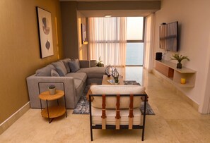 A living room with a sofa, a coffee table, a TV, and a view of the sea. - 25J Lujoso Apto, vista al Oceano Pacífico, 2 rec (Panamá)