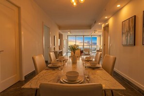 A dining area with a long table set for six, chairs, and a view of the sky through large windows. - 25J Lujoso Apto en YOO, vista al mar con 2 recámaras (Panamá)