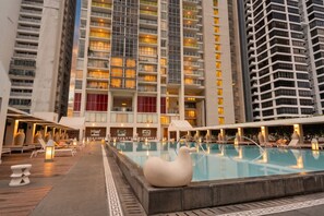 Ein Hotelpool mit großem Becken, Liegestühlen und einem modernen Gebäude im Hintergrund.