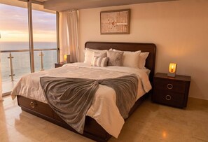 A bedroom with a large bed, a nightstand with a lamp, a view of the sea, and a framed artwork on the wall. - 25J Lujoso Apto, vista al Oceano Pacífico, 2 rec (Panamá)