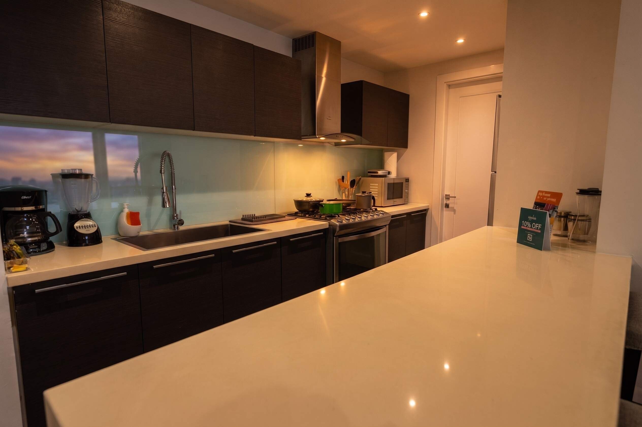 Una cucina moderna con mobili scuri, un piano di lavoro bianco, un fornello integrato, un forno a microonde e una macchina da caffè.