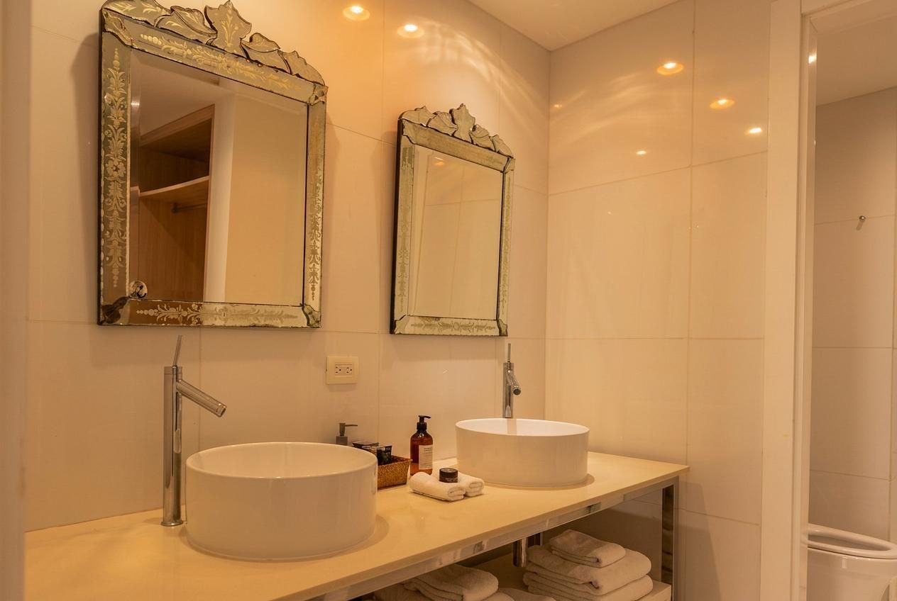 A bathroom with two round white sinks, a mirror with a decorative frame, and a towel rack with folded towels.