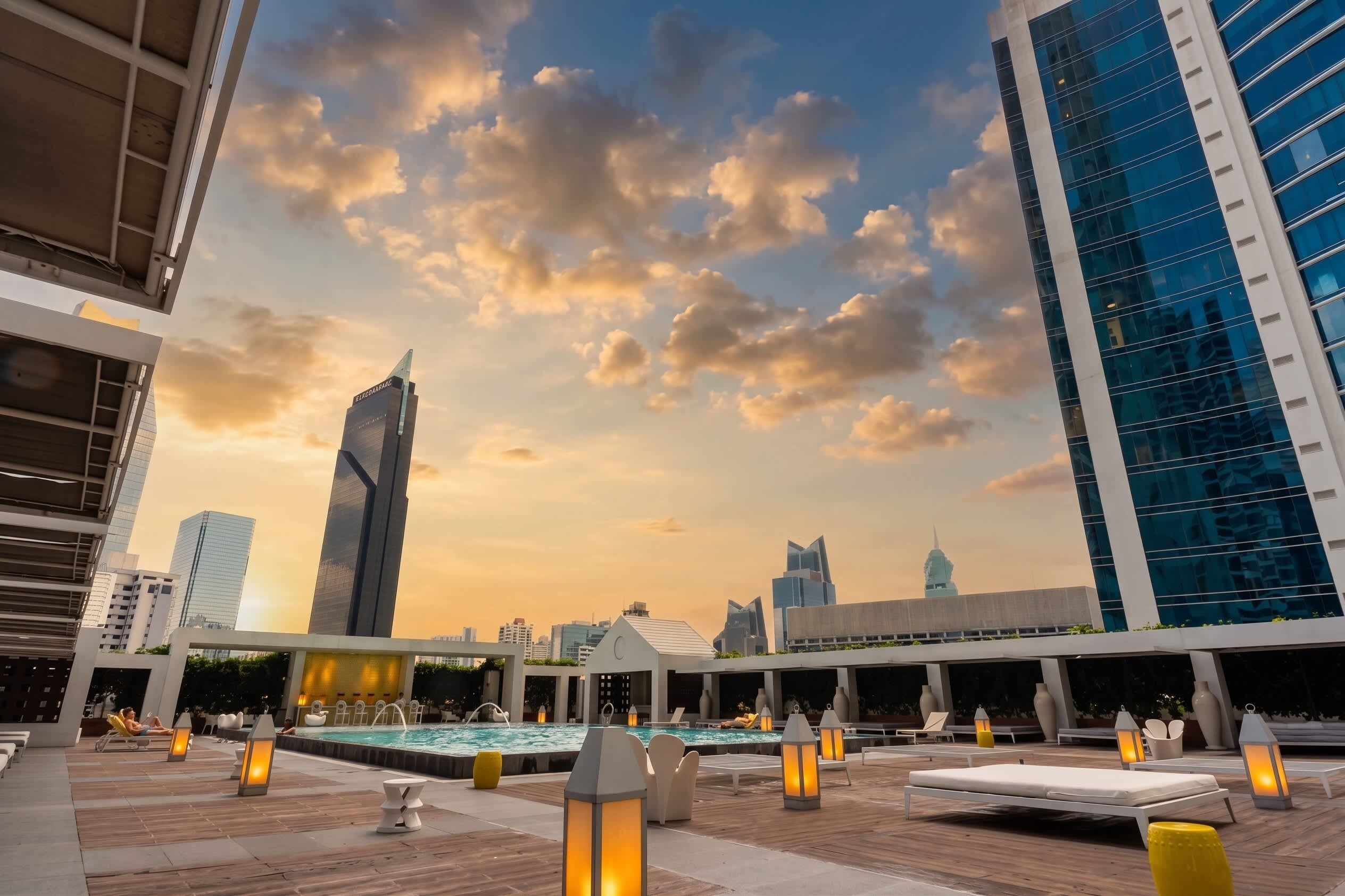 A rooftop pool area with lounge chairs and a view of the city skyline at sunset.