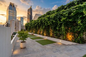 A rooftop garden with a potted tree, a bench, and a pathway leading to a cityscape with modern skyscrapers. - 22J apartamento full equipado vista al mar y 2 hab (Panamá)