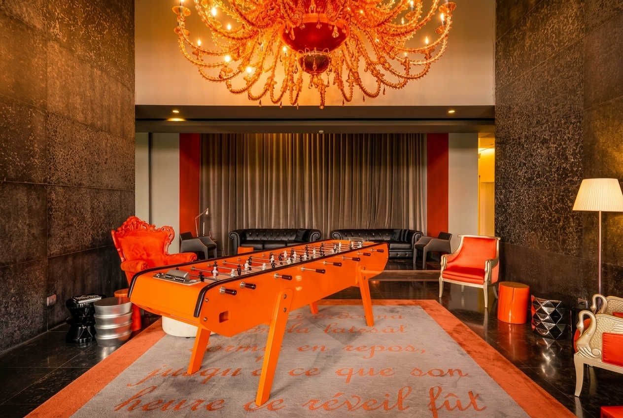Una habitación con mesa de fútbol, candelabro y alfombra roja con texto en francés.