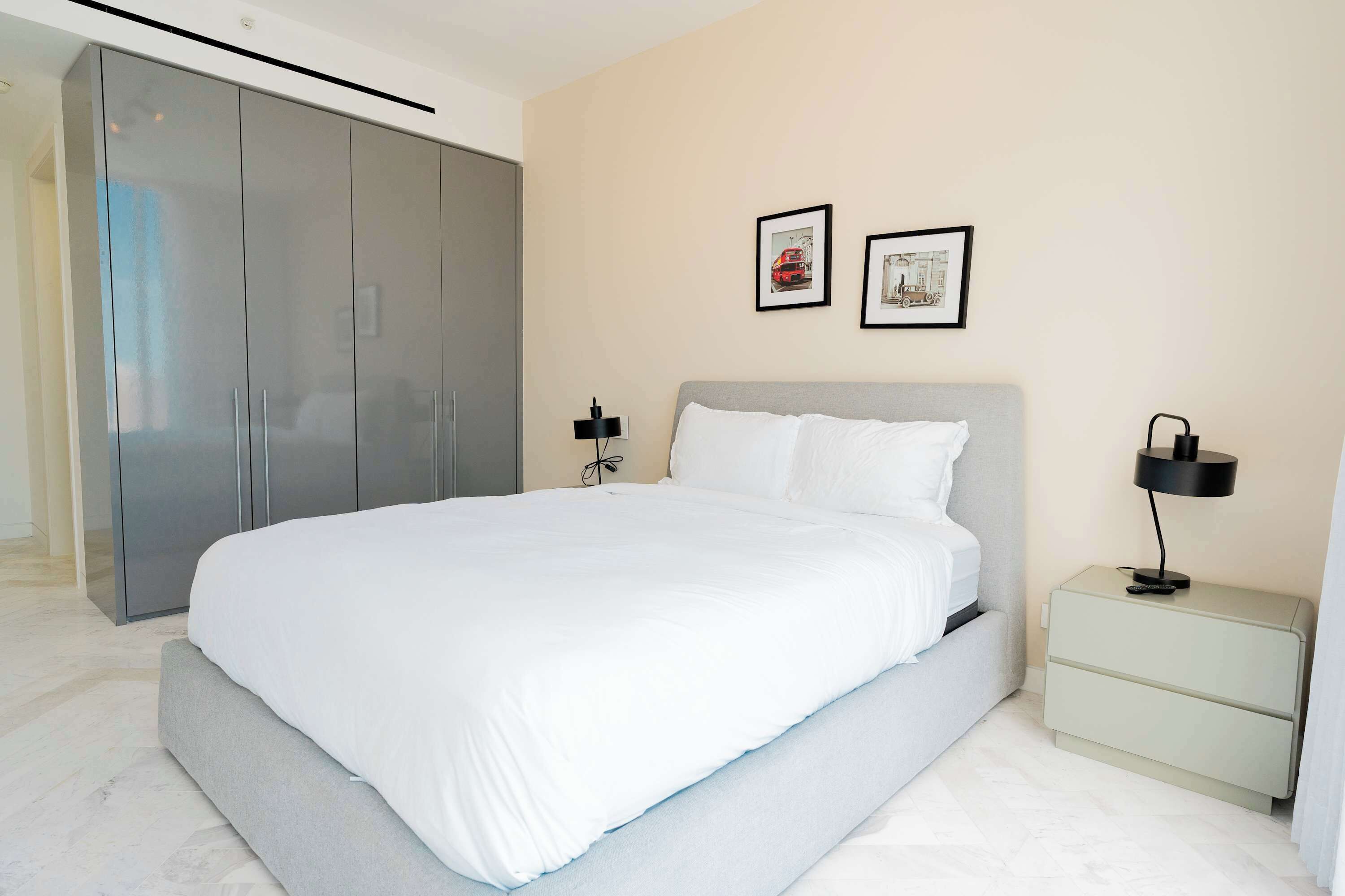 A modern bedroom with a large bed, a wardrobe, a nightstand, and two framed pictures on the wall.