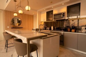 A modern kitchen with a central island, bar stools, a microwave, and a stove. - 24G Apto en Wanders & Yoo Marbella con 3 recamaras (Panama City)