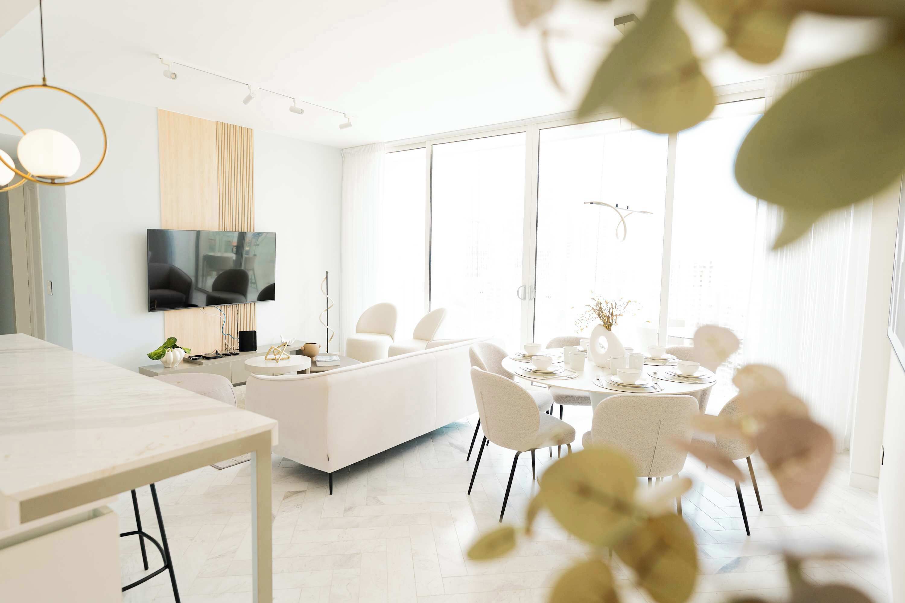 A modern living room with a sofa, dining table, chairs, a TV, and a large window.