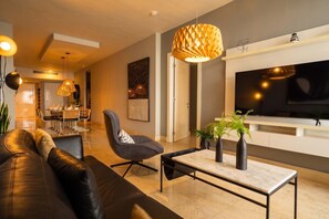 Ein modernes Wohnzimmer mit Sofa, Sessel, Couchtisch und Fernseher.