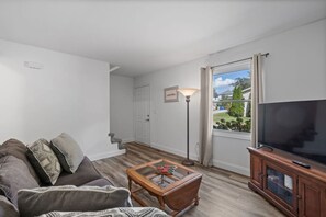 A living room with a sofa, a coffee table, a TV, and a lamp. - Townhouse on Perry - Walk to Main Street (Saint Charles)