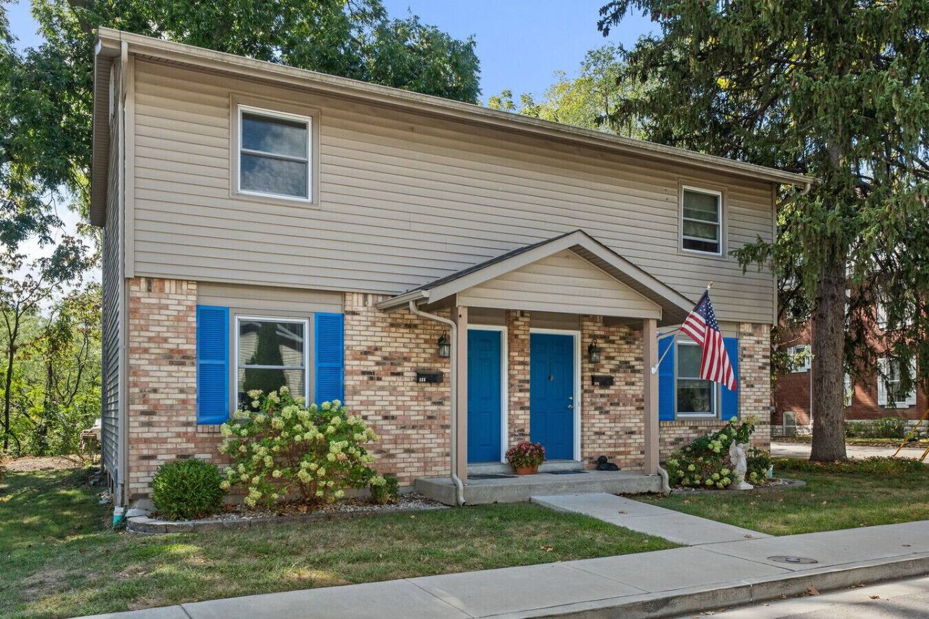 Una casa de dos pisos con fachada de ladrillo, contraventanas azules y una bandera estadounidense.