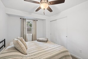 Una camera da letto con un letto, una ventola a soffitto, una finestra con tende e una porta.