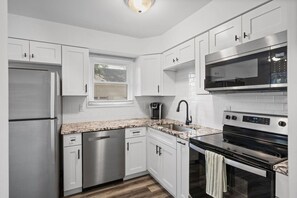 A modern kitchen with stainless steel appliances, white cabinetry, and a window. - Townhouse on Perry - Walk to Main Street (Saint Charles)