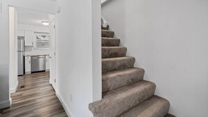 Una escalera con peldaños alfombrados que conduce a una zona de cocina con armarios blancos y un lavavajillas de acero inoxidable.