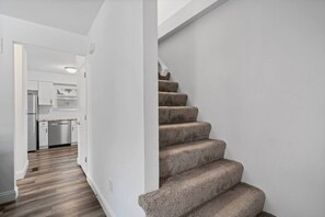 Una scala con gradini rivestiti di moquette conduce a una zona cucina con mobili bianchi e una lavastoviglie in acciaio inossidabile.