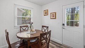 Un comedor con una mesa redonda de madera, cuatro sillas, un jarrón con flores y dos cuadros en la pared.