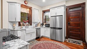 A kitchen with white cabinets, stainless steel appliances, a wooden door, and a red rug. - Oma’s Haus - Walk to Main Street! (Saint Charles)