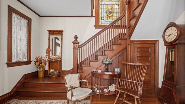A grand staircase with wooden railings, a chandelier, and a large clock. - Oma’s Haus - Walk to Main Street! (Saint Charles)