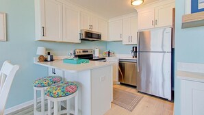 Una cocina con armarios blancos, microondas, tostadora, refrigerador y una pequeña isla con taburetes.