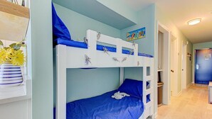 Una cama litera con colchón azul, cabecera blanca y estante superior con figuras decorativas de peces.