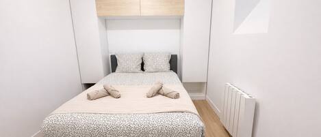 Een smalle hotelkamer met een bed, een inbouwkleerkast en een radiator.