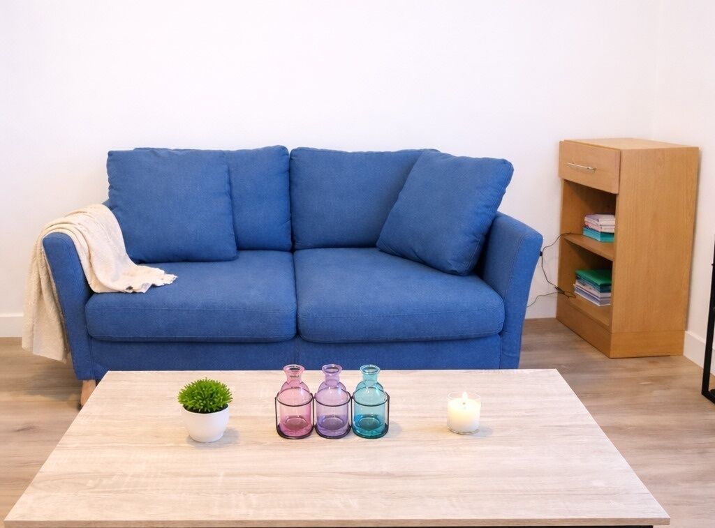 Un sofá azul, una mesa de centro de madera con una planta en maceta, tres jarrones de vidrio y una vela.