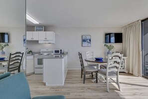 Een moderne keuken met witte kasten, een magnetron en een eethoek met een tafel en stoelen.
