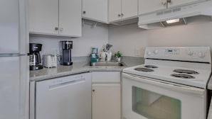 Una cucina compatta con mobili bianchi, un piano cottura bianco, una lavastoviglie e una macchina per il caffè.
