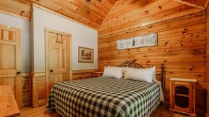 A wooden cabin bedroom with a bed, a small table, and a cabinet. - Porchside Pines։ Private Hot Tub (Pigeon Forge)
