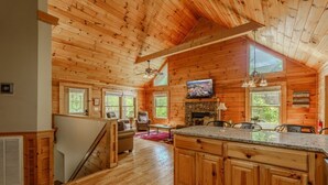 A cabin interior with a wooden interior, a fireplace, a television, and a dining area. - Porchside Pines։ Private Hot Tub (Pigeon Forge)