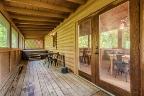 Una terraza cubierta de madera con jacuzzi, mobiliario exterior y vistas al bosque circundante.
