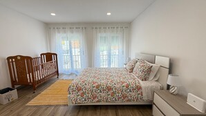 Une chambre à coucher avec un lit, un berceau en bois, une table de chevet avec une lampe et une fenêtre avec des rideaux.