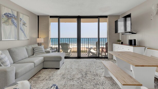 A modern living room with a sofa, a wooden table, and a TV mounted on the wall. - Charming 1 Bedroom Oceanfront Condo in Carolina Beach, perfect for 6 guests 0409 (Carolina Beach)