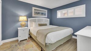 A bedroom with a bed, bedside table, lamp, and artwork on the wall. - Charming 1 Bedroom Oceanfront Condo in Carolina Beach, perfect for 6 guests 0409 (Carolina Beach)