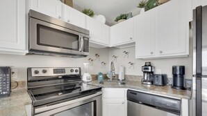 A modern kitchen with stainless steel appliances, white cabinetry, and a granite countertop. - Charming 1 Bedroom Oceanfront Condo in Carolina Beach, perfect for 6 guests 0409 (Carolina Beach)