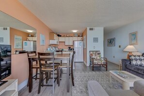 A compact living space with a dining area, kitchen, and seating area. - Experience oceanfront luxury at 0411 Seaside Sunrise, Carolina Beach! (Carolina Beach)