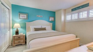 A bedroom with a bed, bedside tables, a lamp, and wall decorations. - Experience oceanfront luxury at 0411 Seaside Sunrise, Carolina Beach! (Carolina Beach)