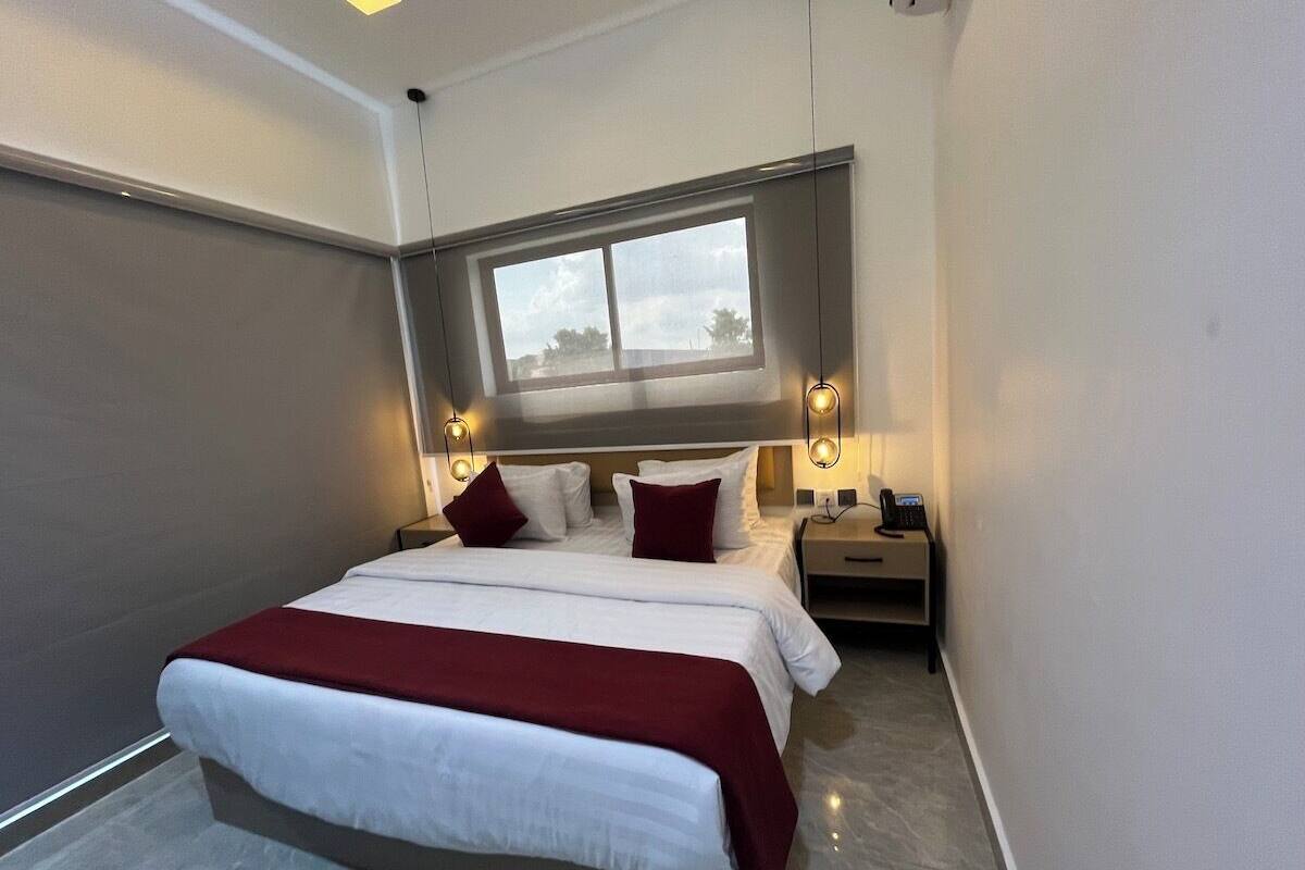 Ett modernt hotellrum med en stor säng, sängbord, ett fönster och ett litet bord.