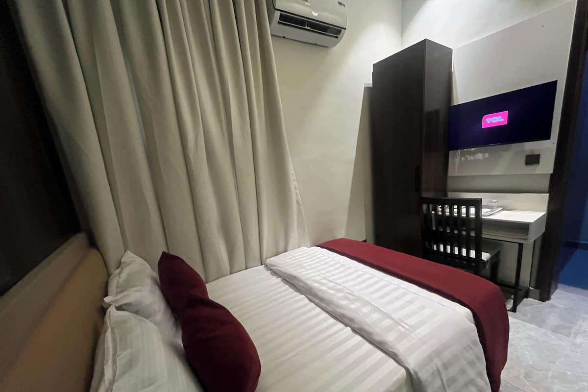 Ett hotellrum med en säng, ett skrivbord, en stol, en TV och en luftkonditioneringsanläggning.